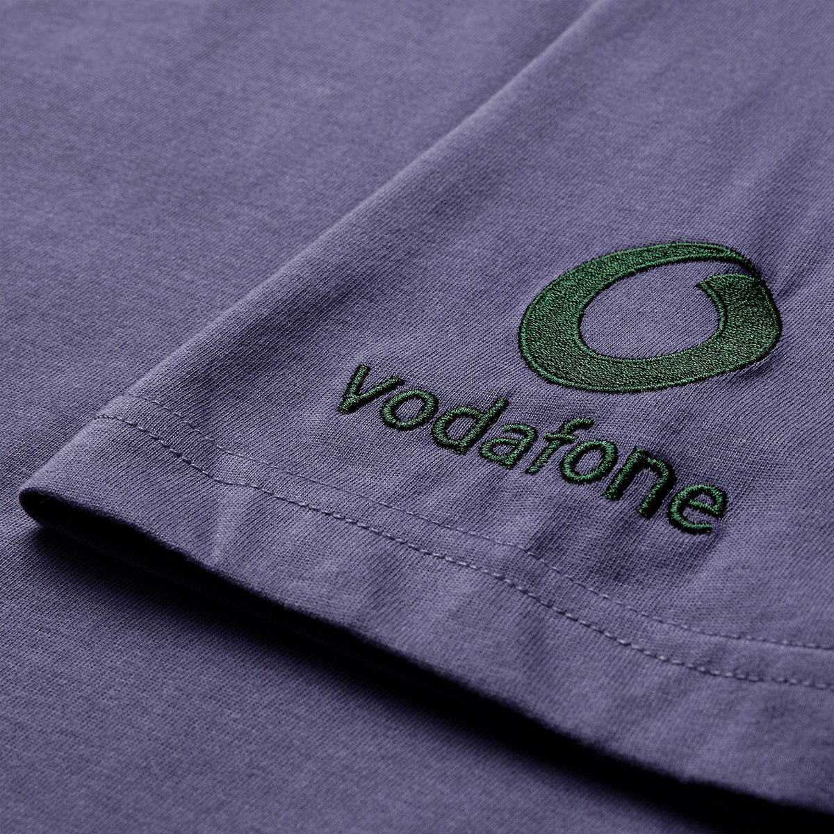 Close-up of a purple fabric featuring the brand logo and name embroidered in green thread near the edge, similar to the detailing on the Canterbury Women’s Ireland 26 Cotton T-shirt.