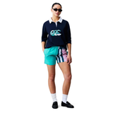 A person wears sunglasses, a navy graphic sweater, Canterbury Uglies Harletic Short in teal and pink stripes, white socks, and black shoes, standing against a white background.