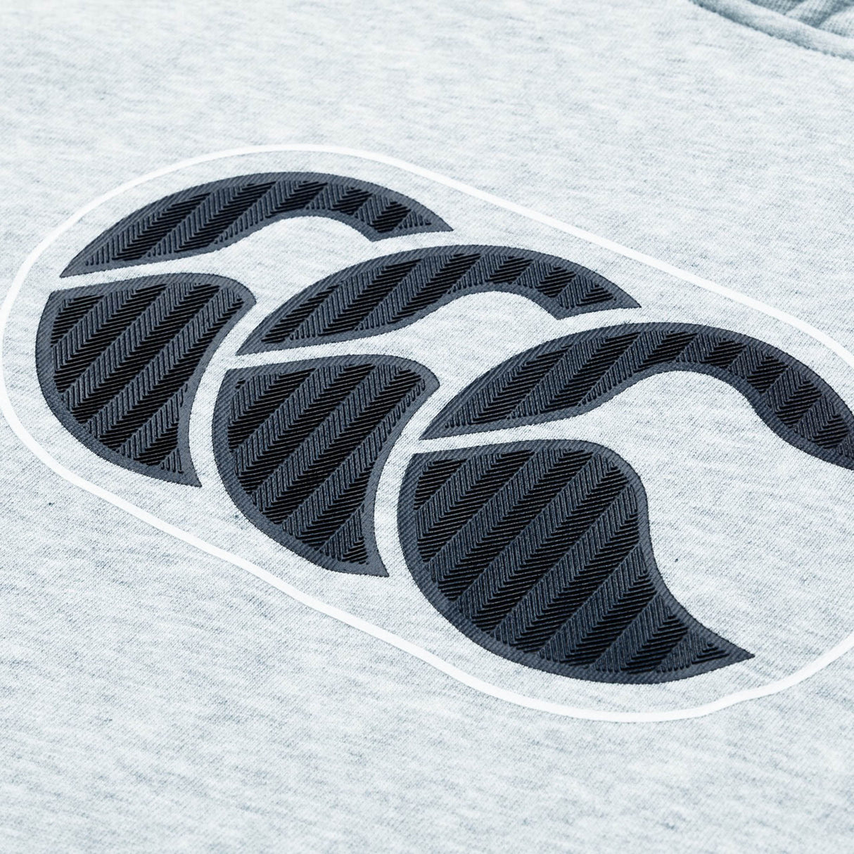 Close-up of the gray fabric on the Women Rakaia 2.0 Hoodie by Canterbury, showcasing a black, textured Canterbury logo with three overlapping stylized C’s.