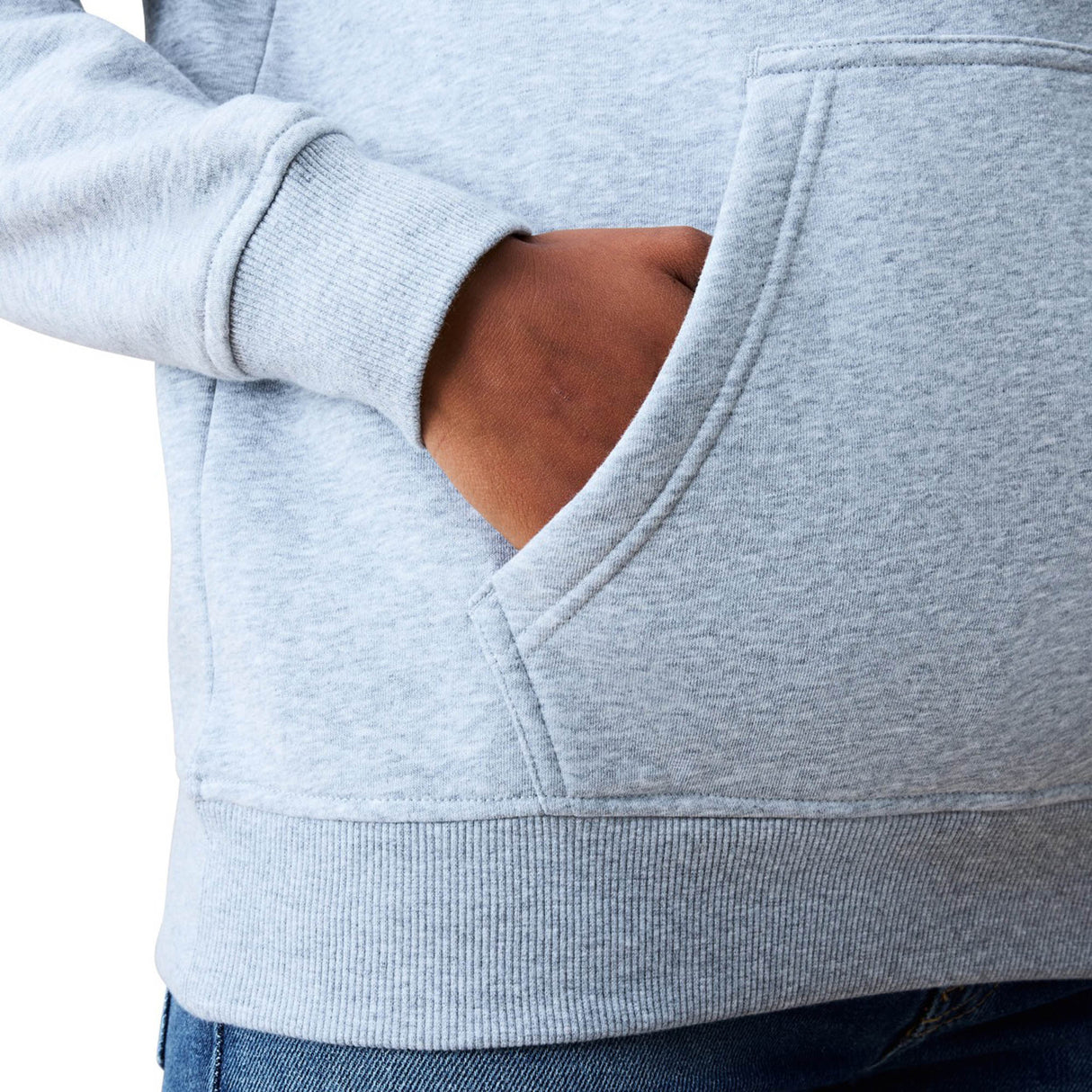 A person wearing a light gray Women Rakaia 2.0 Hoodie by Canterbury and blue jeans places their right hand inside the front pocket of the hoodie.