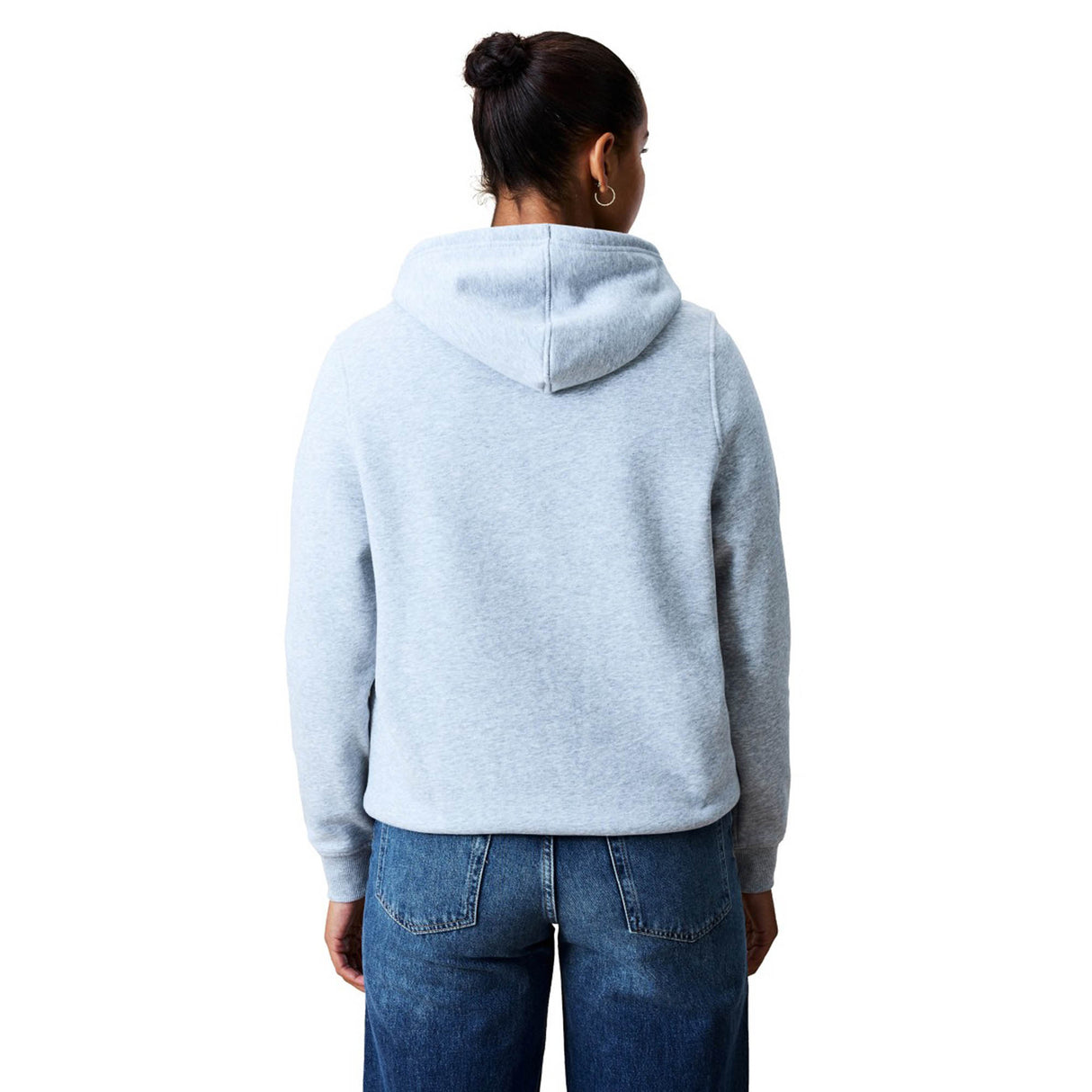 A person stands with their back to the camera, dressed in a light gray Women Rakaia 2.0 Hoodie by Canterbury and blue jeans, set against a white background.