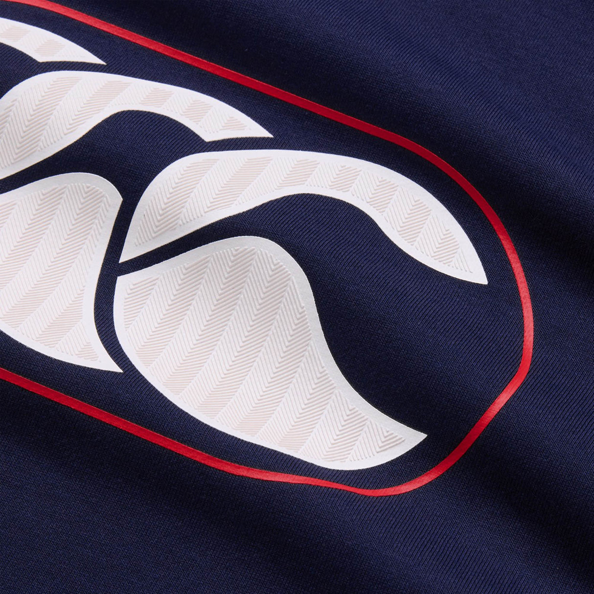 Close-up of the navy blue fabric from the Canterbury Rakaia 2.0 Hoodie by Canterbury, highlighting a white and red logo with curved elements and chevron-like detailing on the white sections.