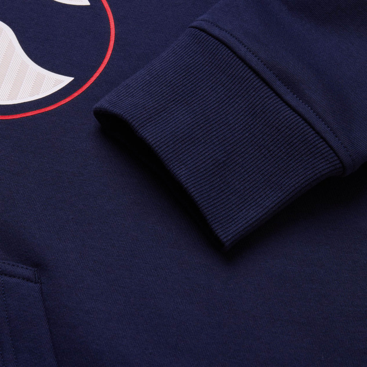 Close-up of a navy blue Canterbury Rakaia 2.0 Hoodie sleeve, showcasing the ribbed cuff and part of a printed red and white graphic.