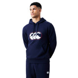 A man wearing a navy blue Canterbury Rakaia 2.0 Hoodie and matching pants, featuring a white Canterbury logo on the chest of the hoodie and the upper left leg of the pants.