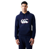 A man stands against a plain white background wearing the Canterbury Rakaia 2.0 Hoodie in navy blue, featuring a white and red Canterbury logo on the chest, paired with matching navy sweatpants.