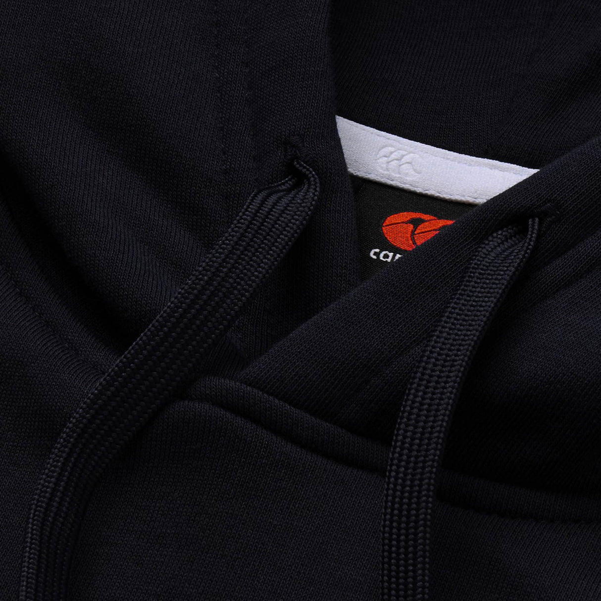Close-up of the Canterbury Rakaia 2.0 Hoodie in black, highlighting the hood drawstrings, fabric texture, and a partially visible tag featuring Canterbury’s iconic red and white logo—a signature detail of this classic rugby hoodie.