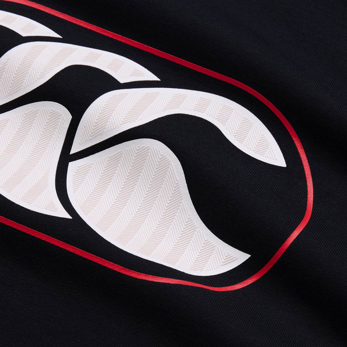 Close-up of a white stylized logo with a red outline on black fabric, highlighting the intricate texture and pattern within the logo—an iconic feature of the Canterbury Rakaia 2.0 Hoodie by Canterbury, ideal for rugby hoodie enthusiasts.