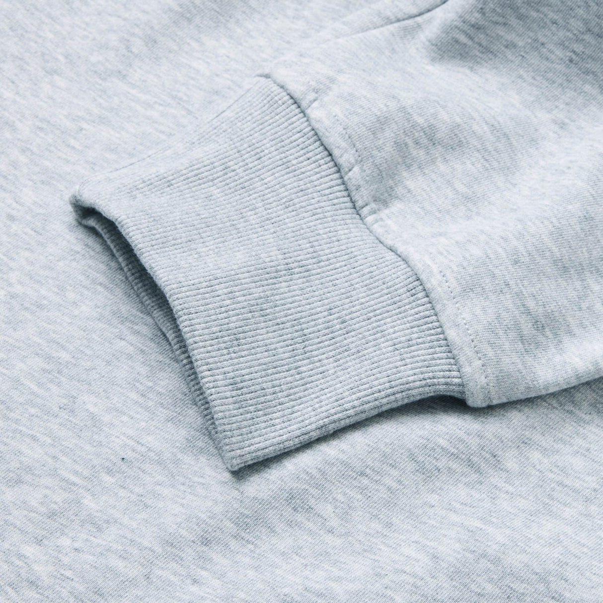 Close-up of a light gray sweatshirt sleeve with ribbed cuff lying flat on a matching gray surface, perfectly complementing the relaxed style of the Canterbury Rakaia 2.0 Fleece Pant.