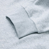 Close-up of a light gray sweatshirt sleeve with ribbed cuff lying flat on a matching gray surface, perfectly complementing the relaxed style of the Canterbury Rakaia 2.0 Fleece Pant.