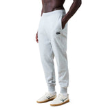 A person wearing light grey Canterbury Rakaia 2.0 Fleece Pant, featuring a black logo on the left thigh, white sneakers, and a bare upper body stands with hands in pockets against a white background.