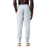 A person standing with their back to the camera is wearing light gray Rakaia 2.0 Fleece Pant by Canterbury and white sneakers against a plain background.