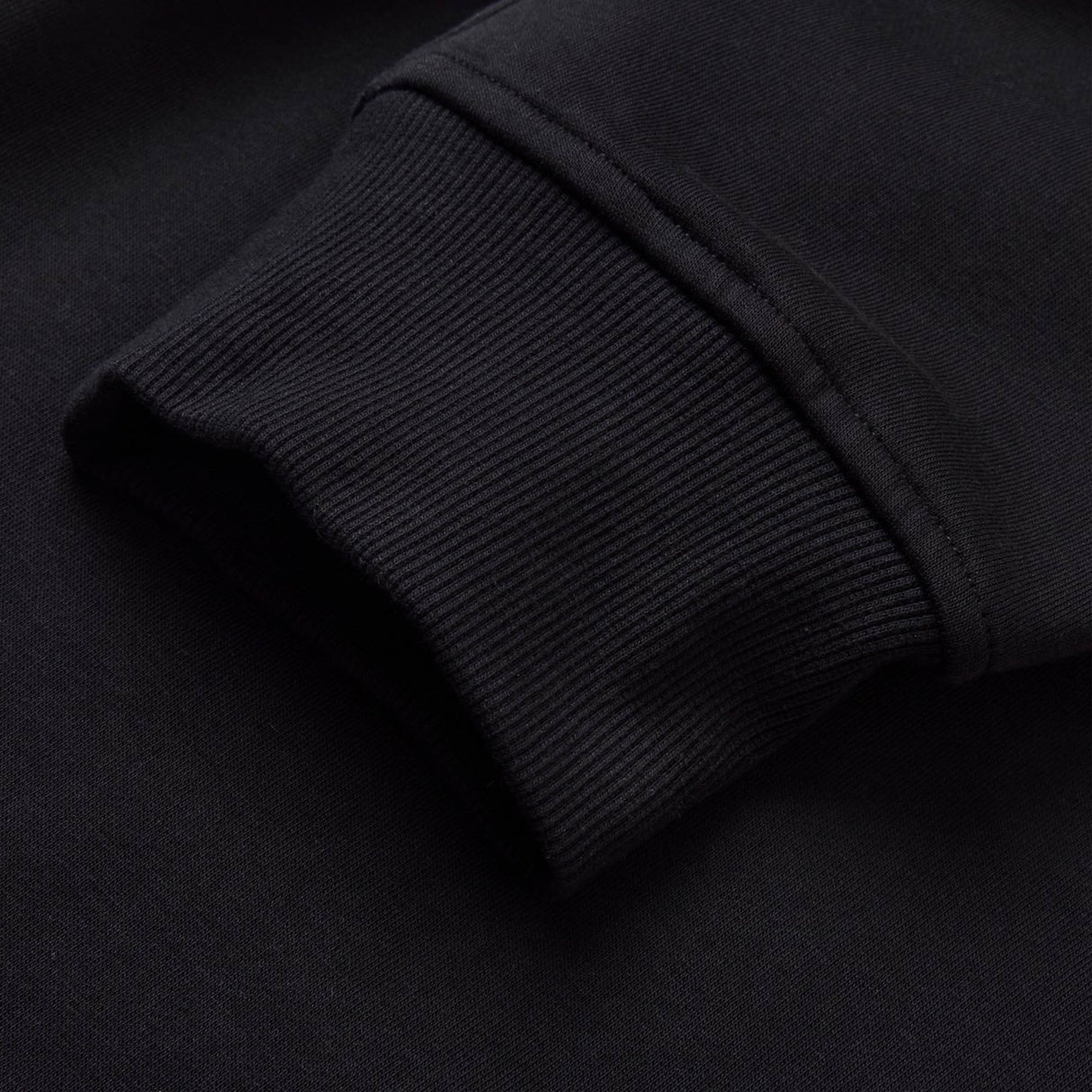 Close-up of a black ribbed sweatshirt cuff resting on a matching black fabric background, evoking the sleek style featured in Canterbury’s Rakaia 2.0 Fleece Pant.