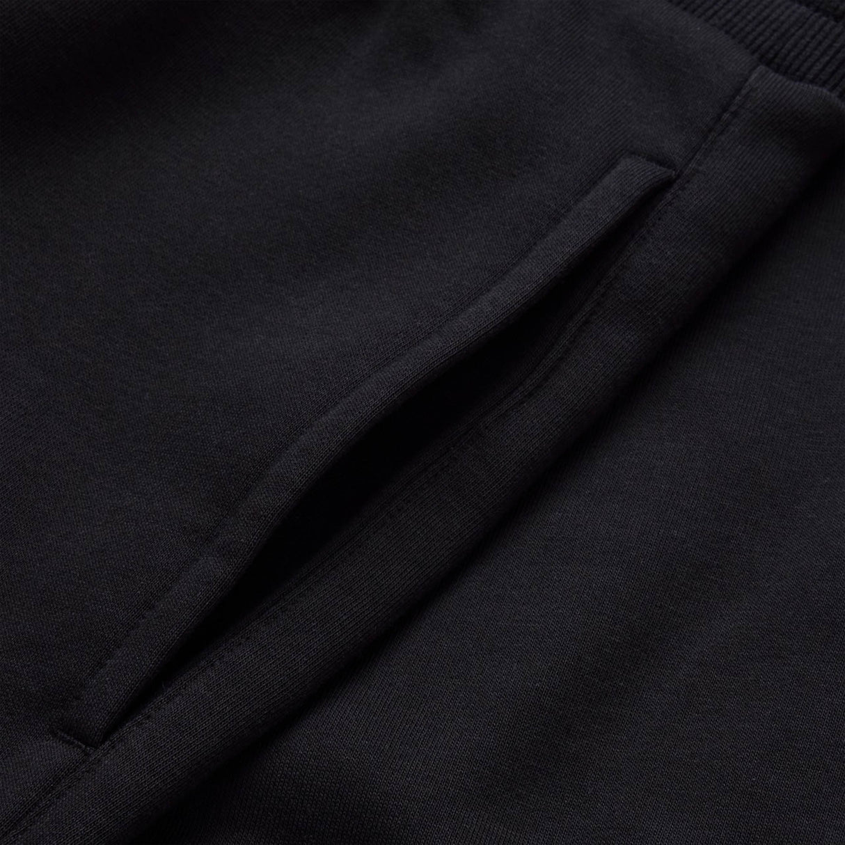 Close-up of a black fabric garment, showing a slanted pocket opening with visible stitching detail, as seen on the Canterbury Rakaia 2.0 Fleece Pant.