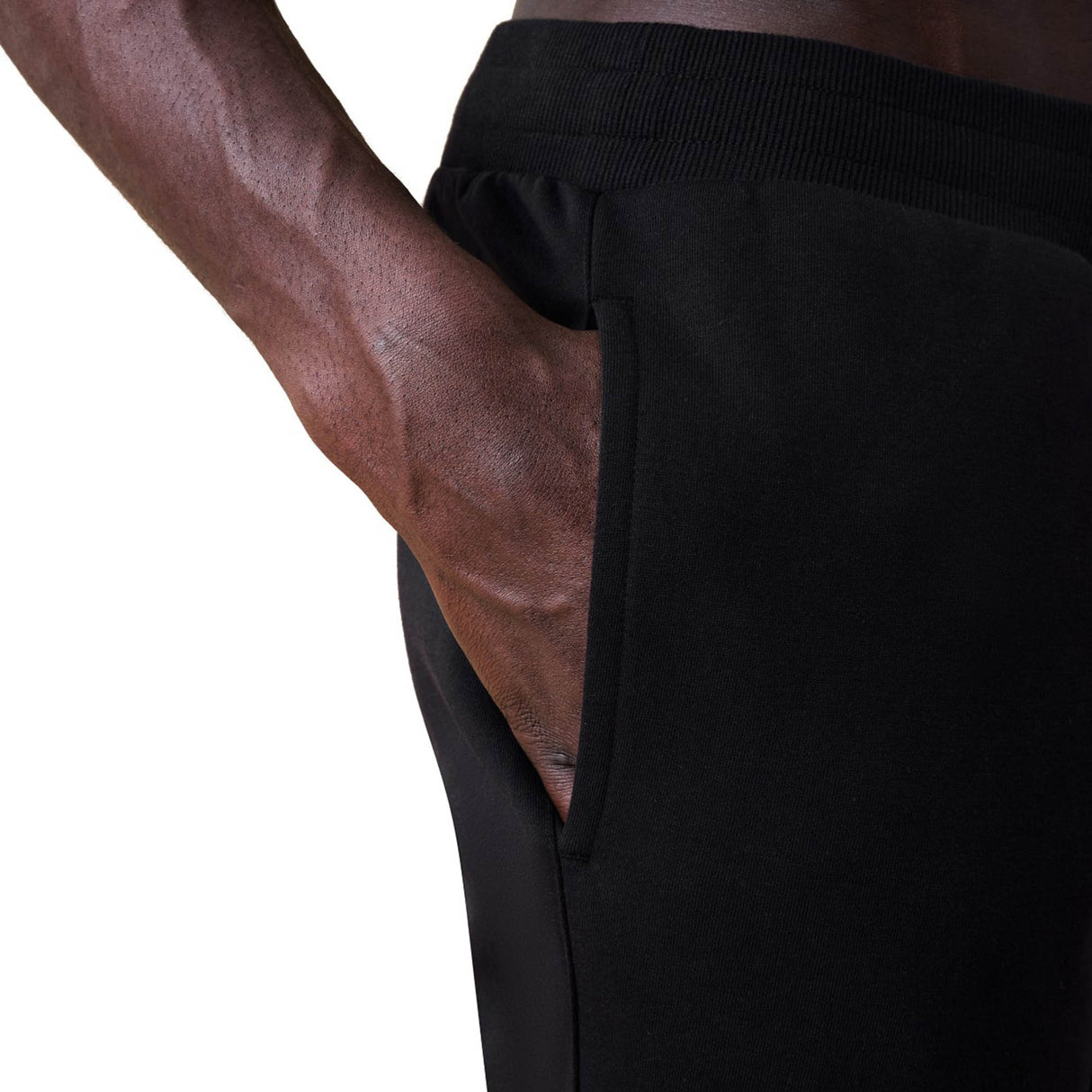 A person wearing black Canterbury Rakaia 2.0 Fleece Pants has their right hand placed inside the side pocket.