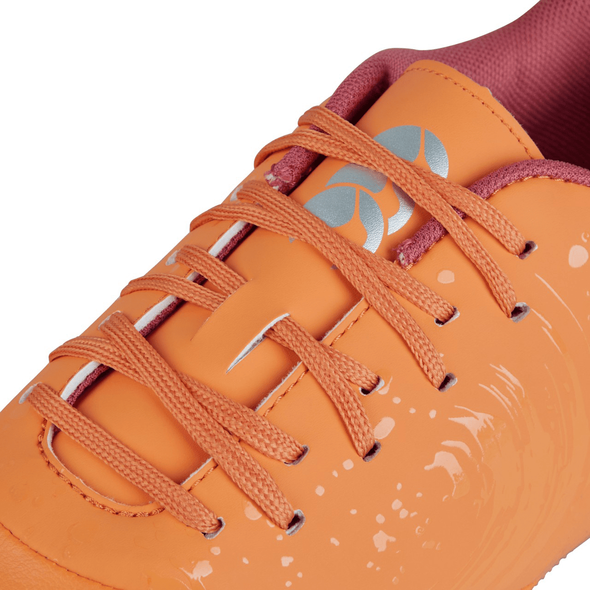 Close-up of the Canterbury Phoenix Genesis Pro SG in Orange Crush/Amber Yellow/Mars Dust, featuring orange laces, a white logo on the tongue, and a splatter paint design on the side. These sneakers boast ultimate traction for any adventure.