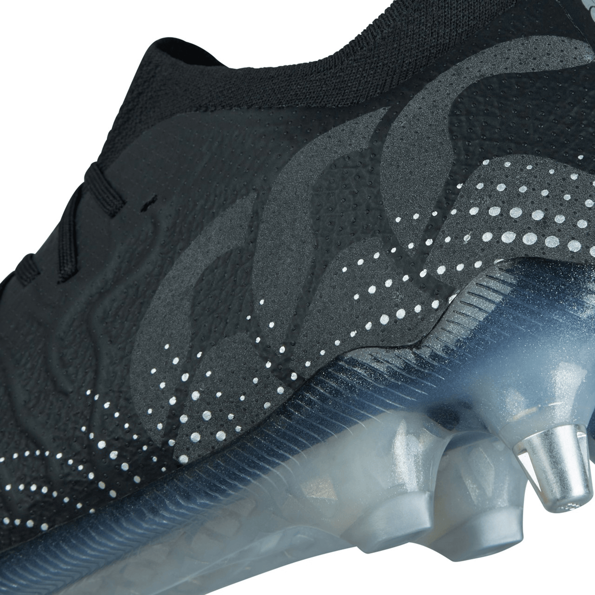 Close-up image of the Canterbury Speed Infinite Elite SG in Black/Silver Metallic, showcasing white dot patterns and a transparent sole with silver studs.