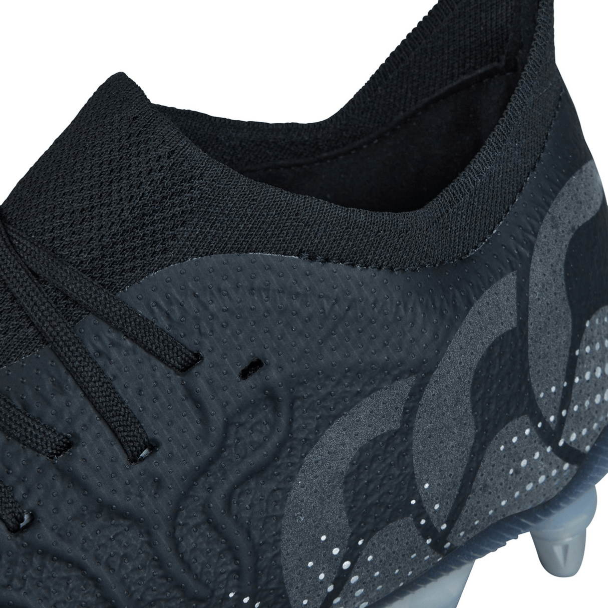 Close-up of the Canterbury Speed Infinite Elite SG - Black/Silver Metallic athletic shoe featuring a textured upper, intricate stitching, and decorative Black/Silver Metallic pattern on the side with black laces and a partially visible clear sole from the renowned brand Canterbury.