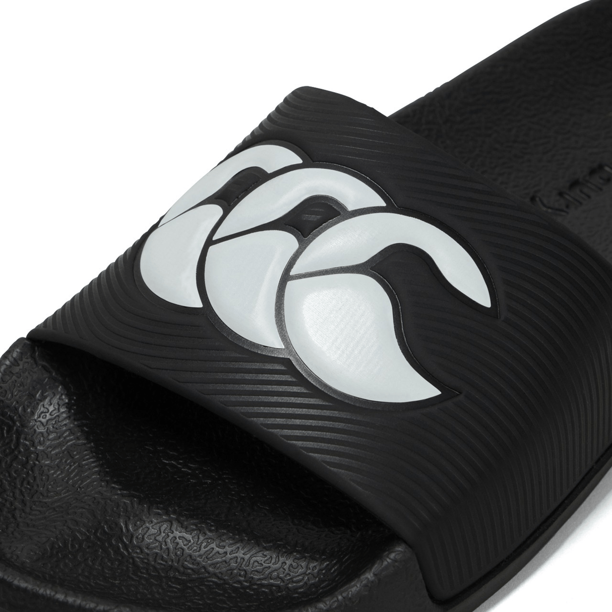 Close-up of the Canterbury Wide Fit Slide - Black sandal front portion, showcasing a white stylized wave pattern on the strap, designed by Canterbury for all-day comfort.