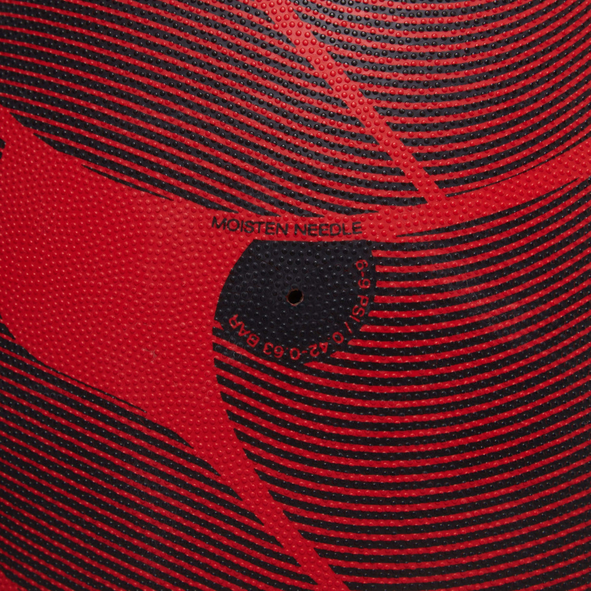 Close-up of a red and black textured Canterbury Thrillseeker Play rugby ball with "moisten needle" text and calibration markings.