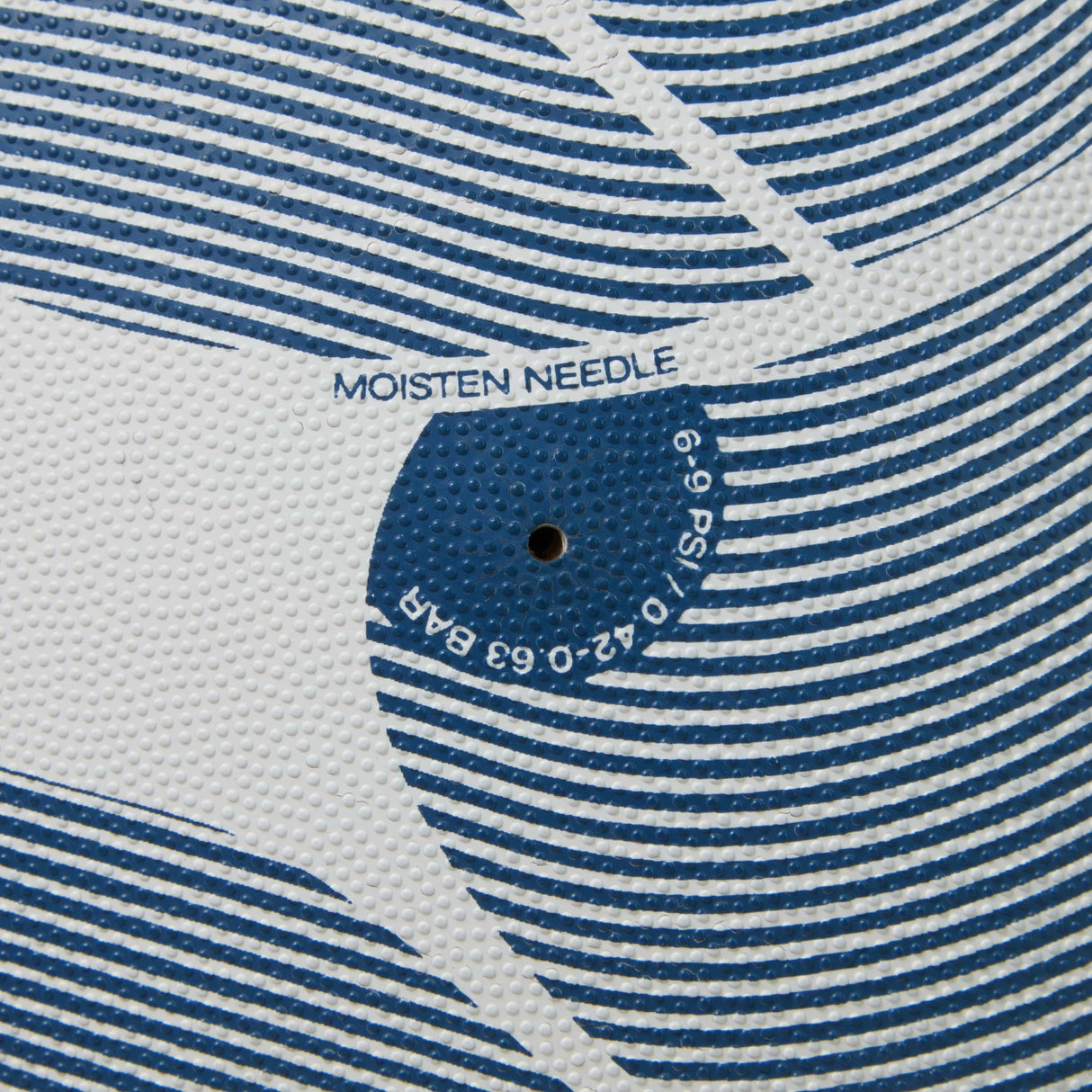 Close-up of a textured surface with concentric circles and text that reads "moisten needle" above a puncture hole on a Canterbury Thrillseeker Play Rugby Ball.