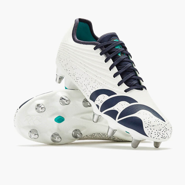 The Canterbury Stampede Groundbreak Pro SG AU-WHITE/BALTIC GREEN rugby boots by Canterbury, featuring a white base with Baltic green accents, metal studs, and a speckled design, are displayed on a plain background—these premium soft ground boots deliver the grip and support needed for scrum specialists.