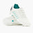 A pair of Canterbury Phoenix 2.0 Pro SG rugby boots in WHITE/BALTIC GREEN, featuring white uppers with baltic green accents and metal studs—one shoe standing on its heel, the other lying sole up—set against a plain white background. Ideal for forwards seeking top performance on soft ground.