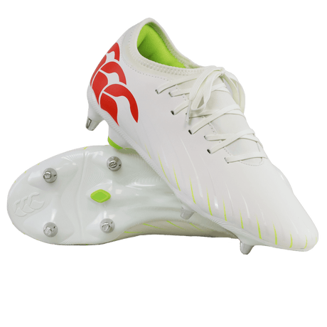 A pair of Canterbury Speed Falcon Team SG soccer cleats in Snow White/Tangerine Tango, featuring a red logo, neon green interior, and metal studs; one shoe stands upright while the other shows its sole.