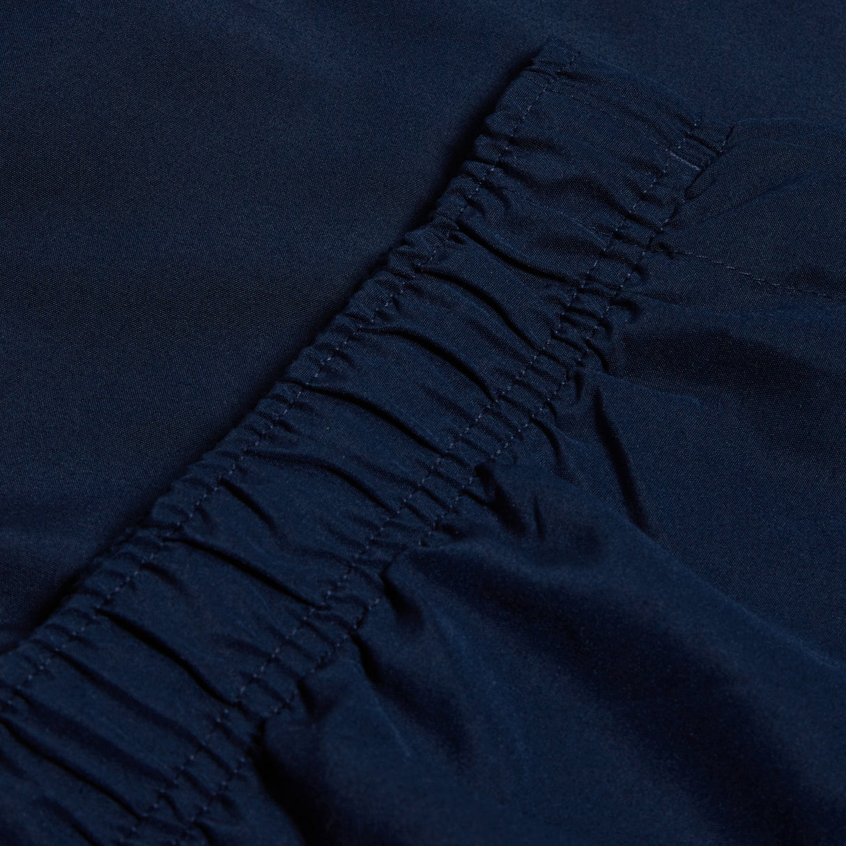 Close-up of dark blue fabric with gathered elastic stitching, reminiscent of a Canterbury logo design on the Women's Canterbury Open Hem Stadium Pant.