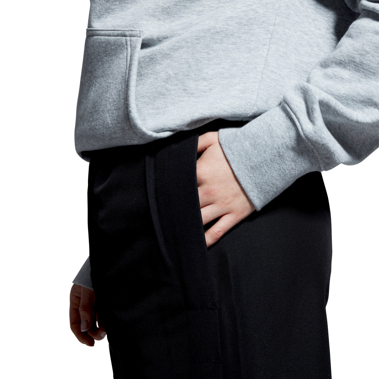 A person wearing a gray hoodie and Women's Canterbury Open Hem Stadium Pant in black, featuring full-length leg zips, with one hand casually tucked in the pant pocket.