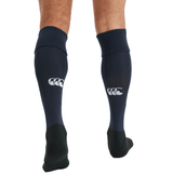Person wearing Canterbury Playing Socks, knee-high in black and navy, featuring a cushioned foot bed and a white Canterbury logo on the back.