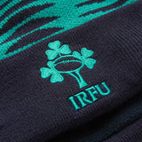Close-up of the Ireland 26 Bobble Hat by Canterbury, featuring a green shamrock and rugby ball logo above the letters “IRFU” on dark knit fabric.