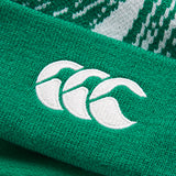 Close-up of a green knit fabric featuring an embroidered white logo with three stylized overlapping shapes, as seen on the Ireland 26 Bobble Hat by Canterbury.