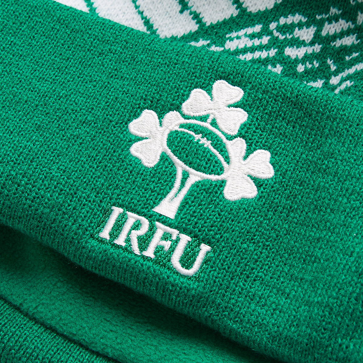 Close-up of a green knit fabric with the IRFU logo—featuring a rugby ball and shamrocks embroidered in white—perfect for an authentic Ireland 26 Bobble Hat by Canterbury.
