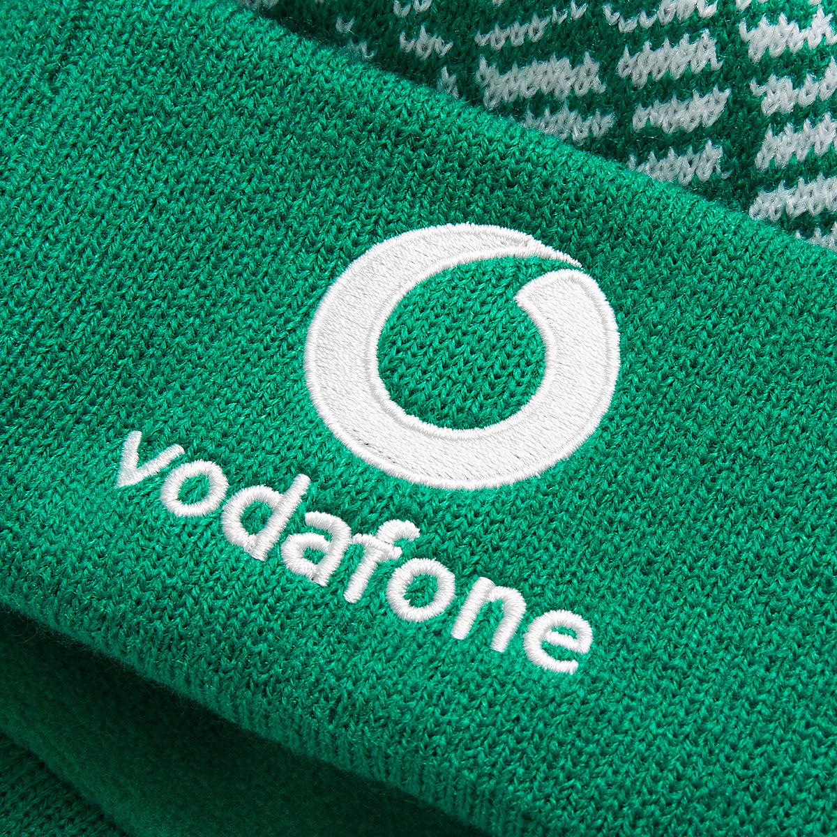 Close-up of green knit fabric with the white Vodafone logo and text embroidered on it, showcasing an authentic Ireland 26 Bobble Hat by Canterbury.