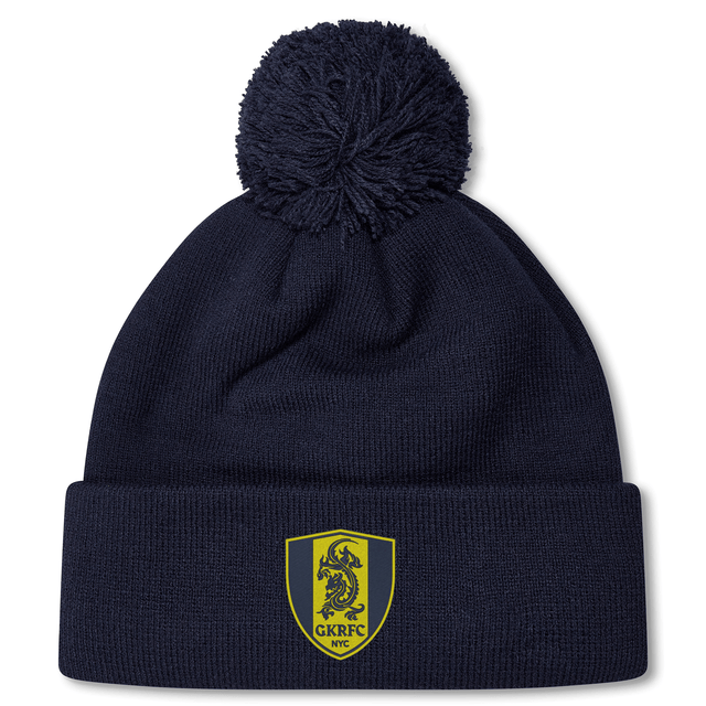The Gotham Knights Pom Pom Beanie by Canterbury from EMB Canterbury is a stylish navy blue knit beanie with a pom-pom on top. It features a yellow and blue shield logo with a dragon and the text "GKRFC NYC." This rugby hat is perfect for keeping warm on cold days out on the field.