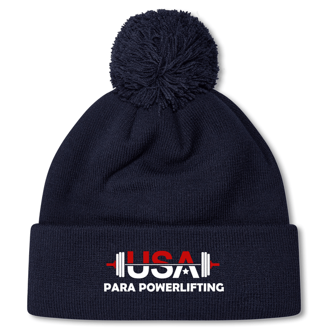 The USA Para Powerlifting Pom Pom Beanie by EMB Canterbury is a navy blue knit beanie with a pom-pom, featuring "USA PARA POWERLIFTING" and a barbell on the front cuff, inspired by classic Rugby style.