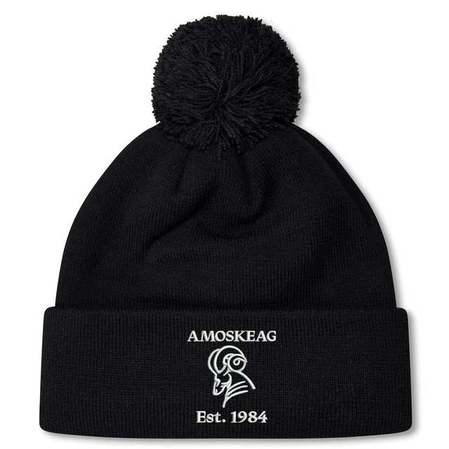 The Amoskeag Rugby Club Pom Pom Beanie by EMB Canterbury is a black knit hat with a folded brim, featuring “AMOSKEAG,” a ram logo, and “Est. 1984” embroidered in white.