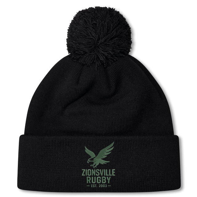 The Zionsville Rugby Club Pom Pom Beanie by EMB Canterbury is a black knit hat with a green eagle and "Zionsville Rugby Est. 2003" on the front cuff, soft fleece lining, and classic pom-pom for added warmth.