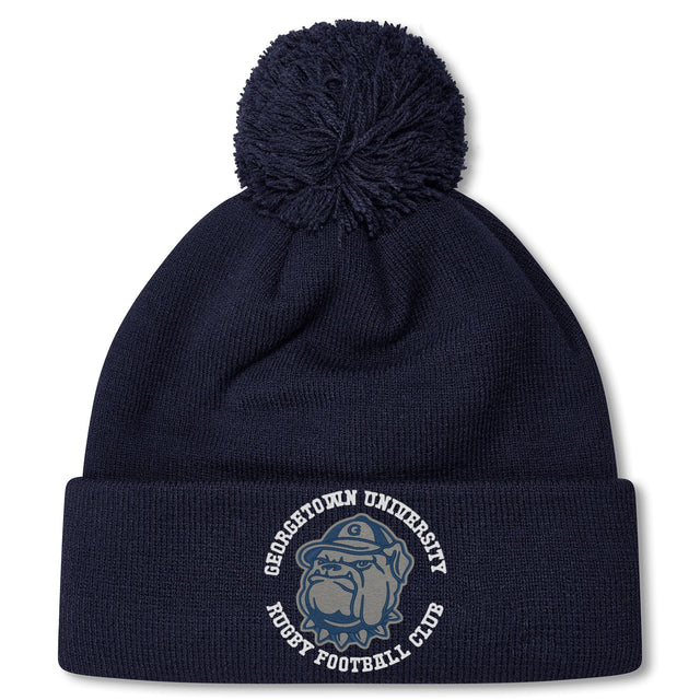 The Georgetown University RFC Pom Pom Beanie by Canterbury features a navy blue knit, fleece lining, pom-pom, bulldog graphic, and club logo—a perfect rugby fan hat from EMB Canterbury.