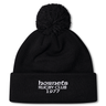 The Hornets Rugby Club 1977 Pom Pom Beanie by Canterbury from EMB Canterbury features a black knit design in the classic Canterbury bobble hat style, with a pom-pom on top and white embroidered "hornets RUGBY CLUB 1977" text on the front cuff.