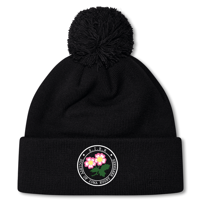The Society of Iowa Rugby Referees Pom Pom Beanie by EMB Canterbury is a black knit fleece-lined beanie topped with a pom-pom, featuring a circular embroidered patch with two pink flowers and border text, combining cozy comfort with the classic rugby beanie style.