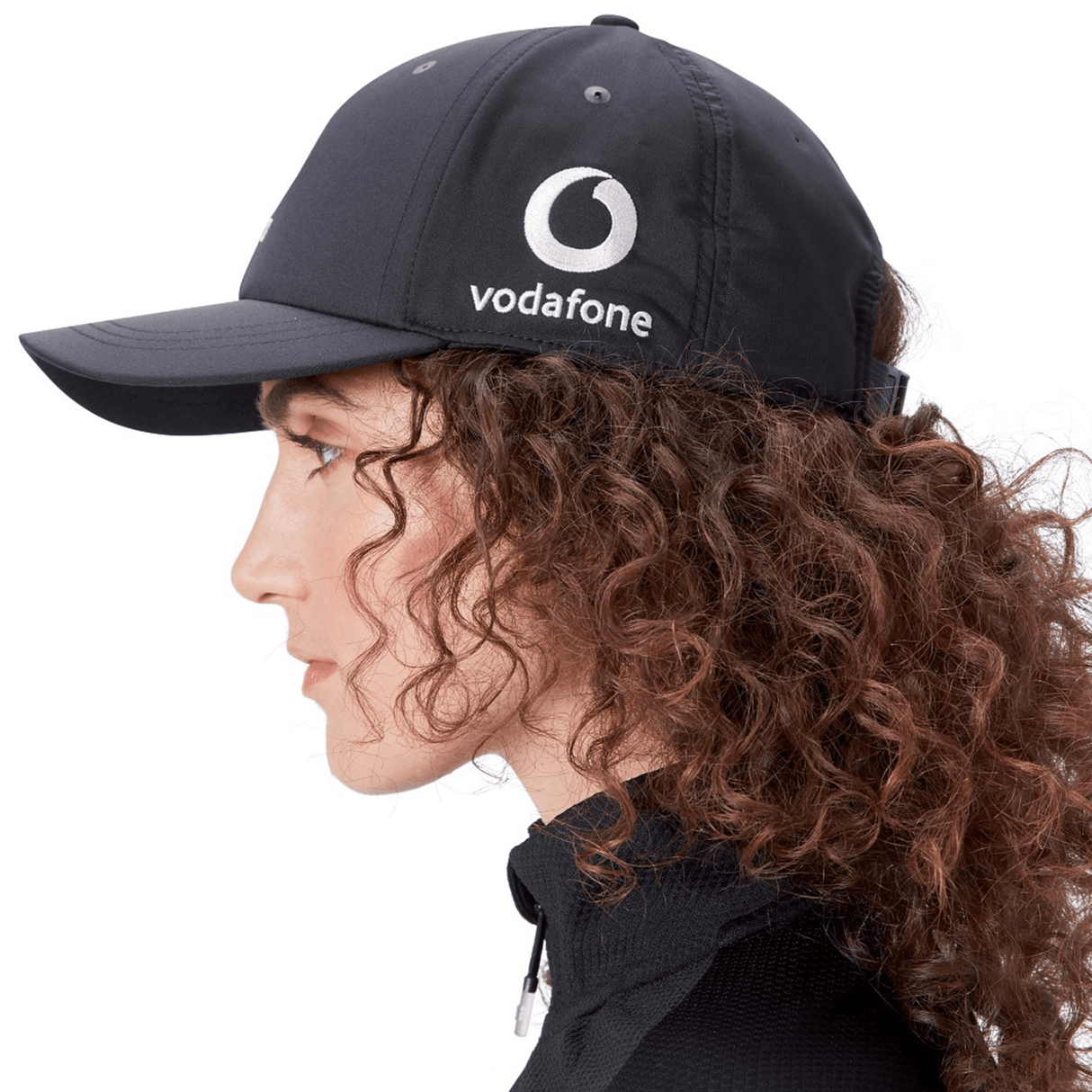 Side profile of a person with curly hair wearing an Ireland 24 Tech Logo Cap by Canterbury, featuring the Vodafone logo and an adjustable strap.