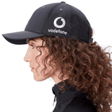 Side profile of a person with curly hair wearing an Ireland 24 Tech Logo Cap by Canterbury, featuring the Vodafone logo and an adjustable strap.