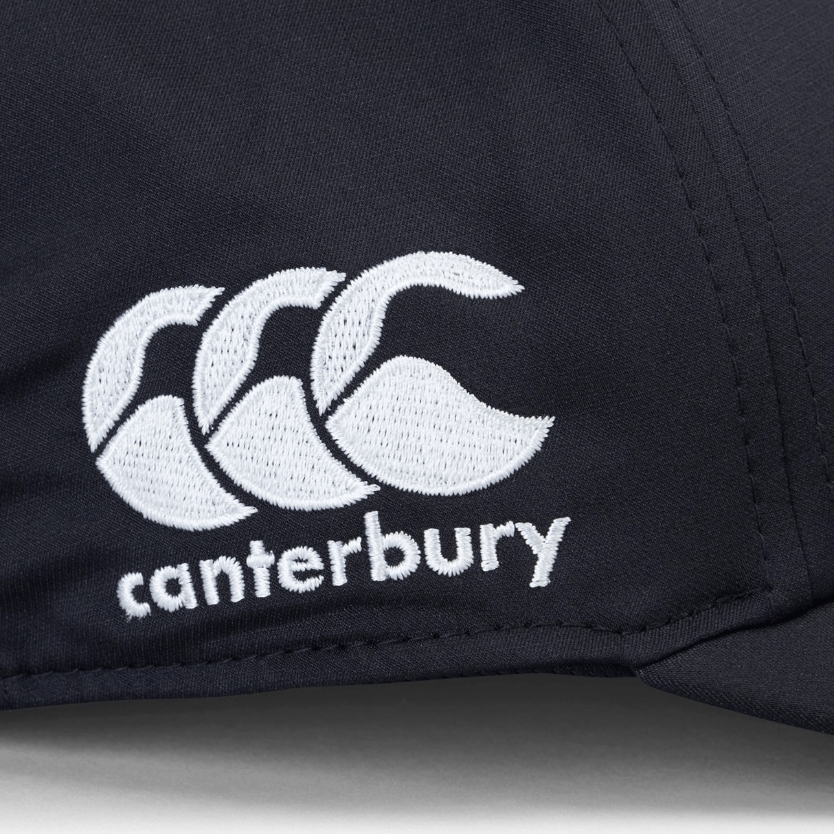 Close-up of the Canterbury logo, featuring three white overlapping curves above the word "canterbury," embroidered on a dark fabric background of the Ireland 24 Tech Logo Cap by Canterbury with an adjustable strap.