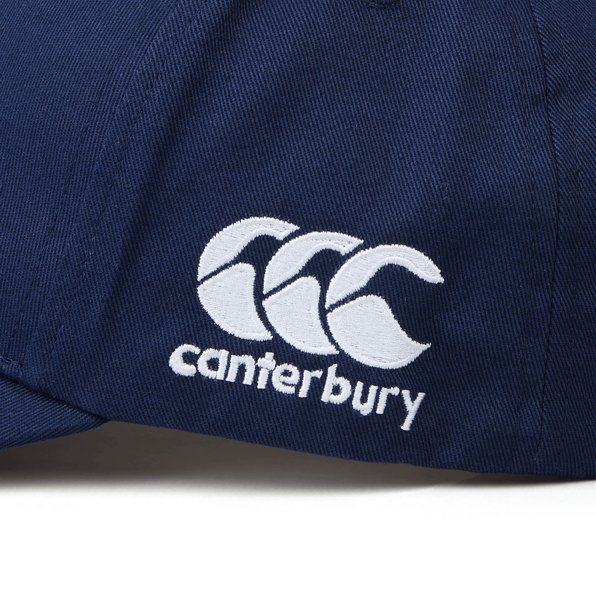 A close-up of the Great Britain Shield Flex Drill Cap in navy blue showcases a white EMB Canterbury logo embroidered on the side. Just In: This chic accessory proudly nods to the Great Britain Shield.