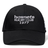 The Hornets Rugby Club 1977 Flexfit Drill Cap by Canterbury features black fabric with white embroidered "hornets RUGBY CLUB 1977" text on the front. This curved brim cap from EMB Canterbury also includes a subtle CCC logo, combining style and comfort for rugby fans.
