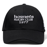 The Hornets Rugby Club 1977 Flexfit Drill Cap by Canterbury features black fabric with white embroidered "hornets RUGBY CLUB 1977" text on the front. This curved brim cap from EMB Canterbury also includes a subtle CCC logo, combining style and comfort for rugby fans.
