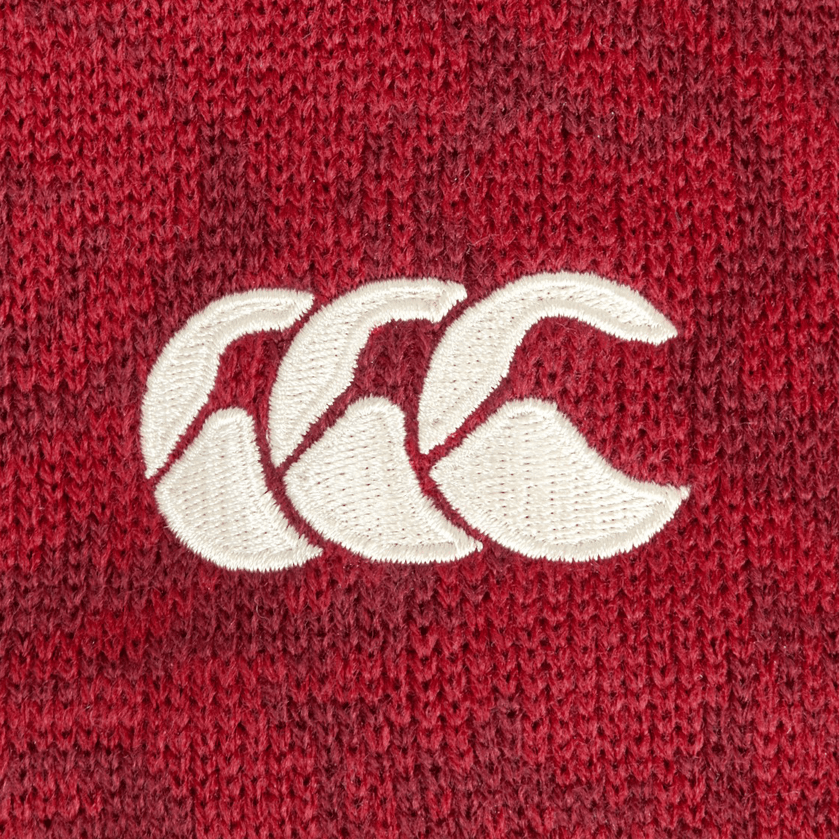 Close-up of a red knitted fabric on the British & Irish Lions 2025 Pom-Pom Beanie by Canterbury, featuring a white embroidered logo with three overlapping stylized C's, reminiscent of the renowned Canterbury style.