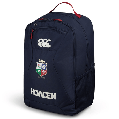 The British & Irish Lions 2025 Medium Backpack by Canterbury in navy blue showcases the Howden logo, the CCC brand logo, and a vibrant multi-color crest. It features two zippered compartments, dual water bottle pockets, a mesh side pocket, and includes a padded laptop sleeve for convenience. The striking red top handle adds both style and functionality.
