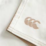 Close-up of Canterbury Fundamental Harlequin Drill 3" Shorts in light beige, featuring tan stitching and a tan three-wave logo printed on the surface.